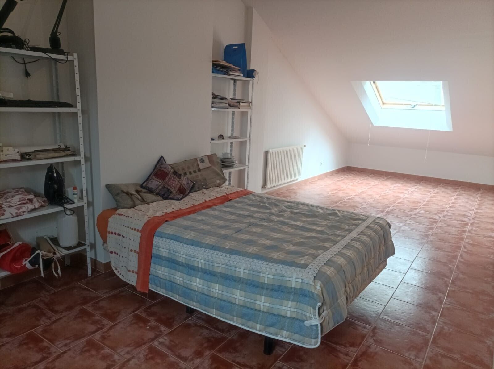 Ein Schlafzimmer mit Bett, Regalen, einer Heizung und einem Oberlicht.