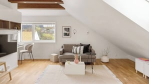Un loft moderne avec un plafond en pente, un canapé gris, une table basse blanche et une grande fenêtre.