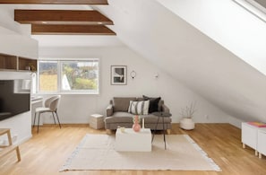 A modern loft with a sloped ceiling, a grey sofa, a white coffee table, and a large window. - Charming Seaside Apartment in Bergen With Stunning Views (Bergen)