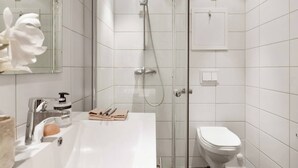 Une salle de bain moderne avec une douche à parois de verre, un lavabo blanc doté d’un distributeur de savon et des toilettes.
