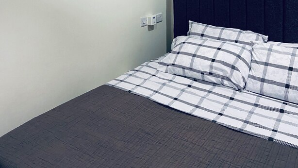 A bed with a checkered bedspread, a wall-mounted air conditioner, and a painting of colorful objects. - Kawe beach Apartments, get a clear city view of Dar es Salaam from your balcony (Dar es Salaam)