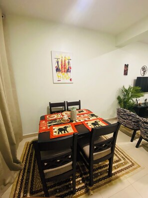 Zona pranzo con tavolo imbandito per quattro persone, sedie, tappeto decorato e opere d'arte alle pareti.