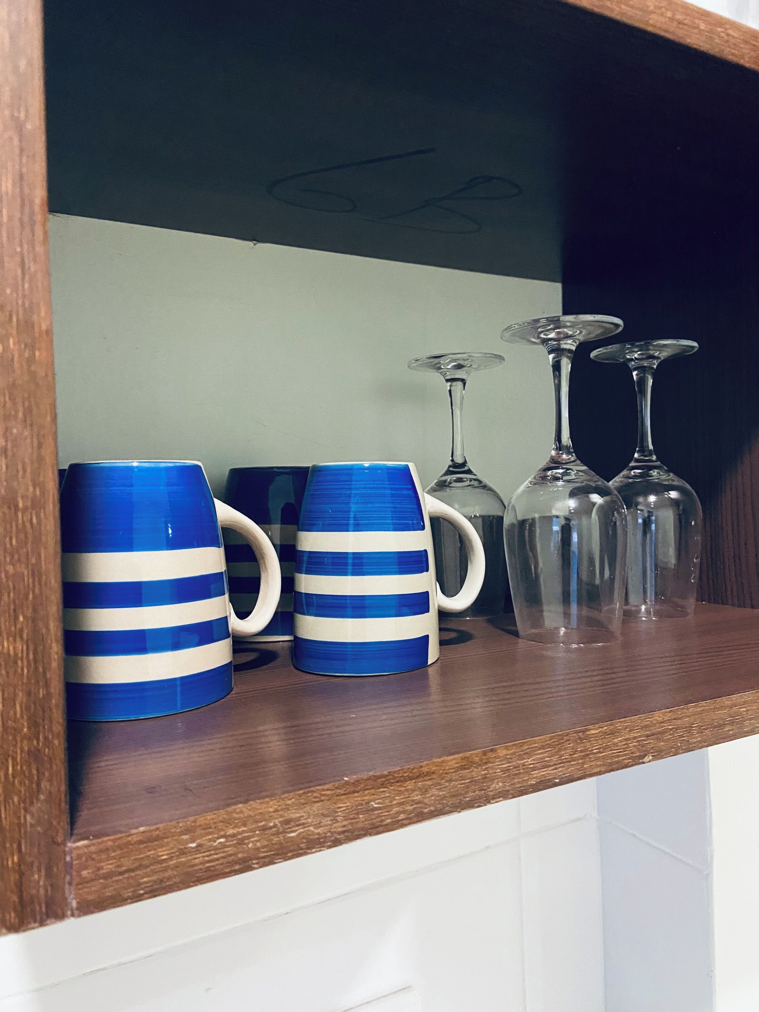 Een plank met twee blauw gestreepte mokken, twee glazen wijnglazen en een helder glas.
