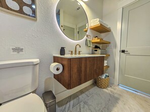 Casa de banho com sanita, lavatório, espelho e prateleiras com toalhas.