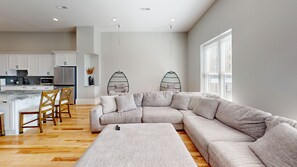 A modern living room with a sectional sofa, a coffee table, and a dining area with chairs and a kitchen in the background.