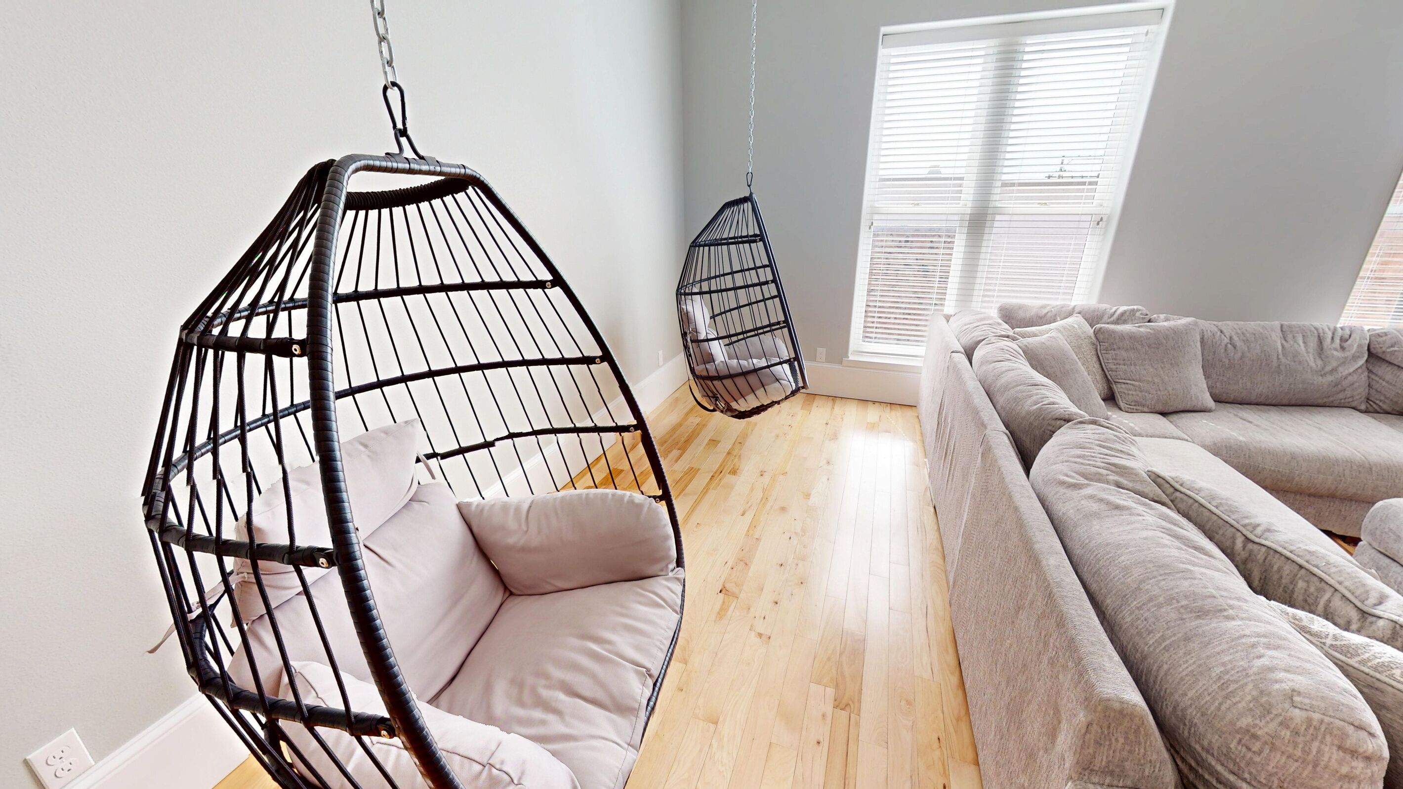 A room with a hanging chair, a sofa, and a window with blinds.