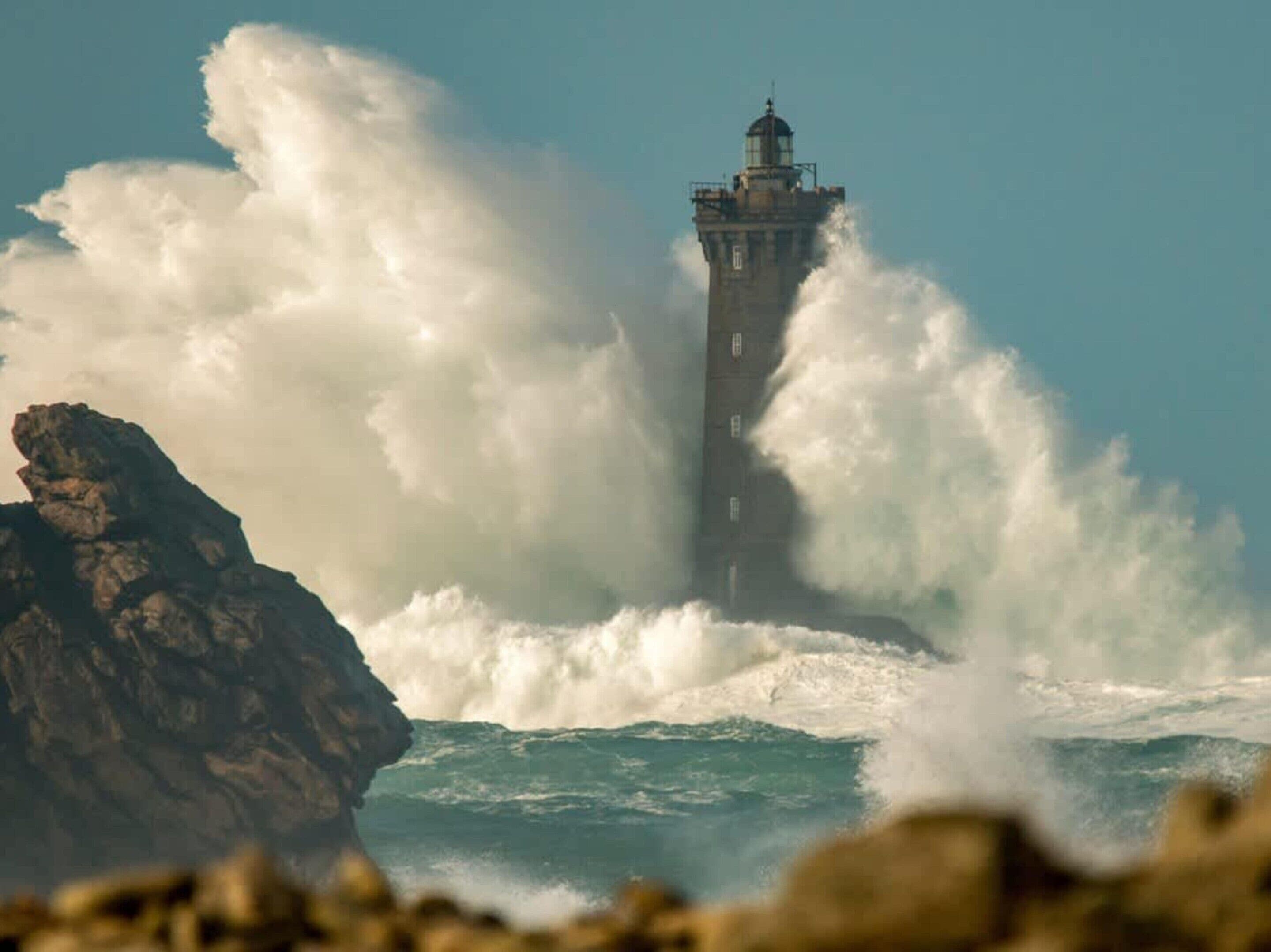 A lighthouse with a rocky foreground and rough sea waves.