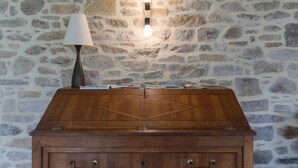 A wooden chest with drawers against a stone wall, a lamp, and a wall-mounted light fixture. - Holiday Home by Lampaul Beach With Garden (Lampaul-Ploudalmézeau)
