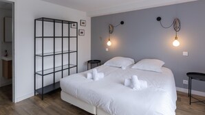 A bedroom with a bed, a black metal shelf unit, two bedside tables, and wall-mounted light fixtures. - Holiday Home by Lampaul Beach With Garden (Lampaul-Ploudalmézeau)