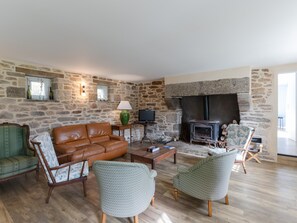 A stone-walled living room with a fireplace, leather sofa, patterned chairs, and a television. - Holiday Home by Lampaul Beach With Garden (Lampaul-Ploudalmézeau)
