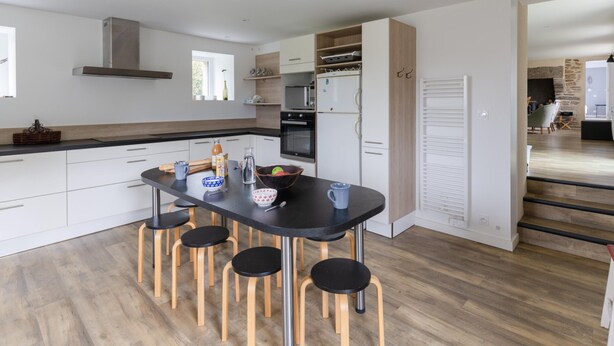 A modern kitchen with a central island, wooden stools, and a view into the living area. - Holiday Home by Lampaul Beach With Garden (Lampaul-Ploudalmézeau)