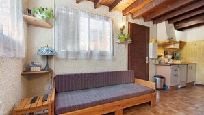 Ein gemütliches Zimmer mit einer Holzbank, einem kleinen Tisch mit Lampe, einem Fenster mit leichtem Vorhang und einer Küchenzeile mit Schränken und Spüle.