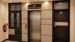 Entrada de ascensor con un letrero que dice 'The White Tulip', un extintor y una alfombra de bienvenida.