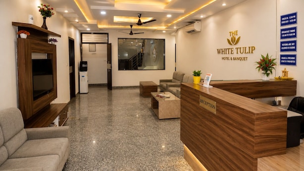 A hotel reception area with a reception desk, sofas, a TV, and a wall-mounted sign. - Hotel The White Tulip (Jaipur)