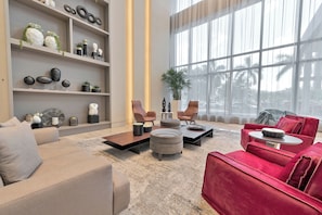 A modern living room with a sofa, ottoman, and chairs, a coffee table, and a bookshelf with decorative items. - Modern 2BR Residence with open views & Balcony (Doral)