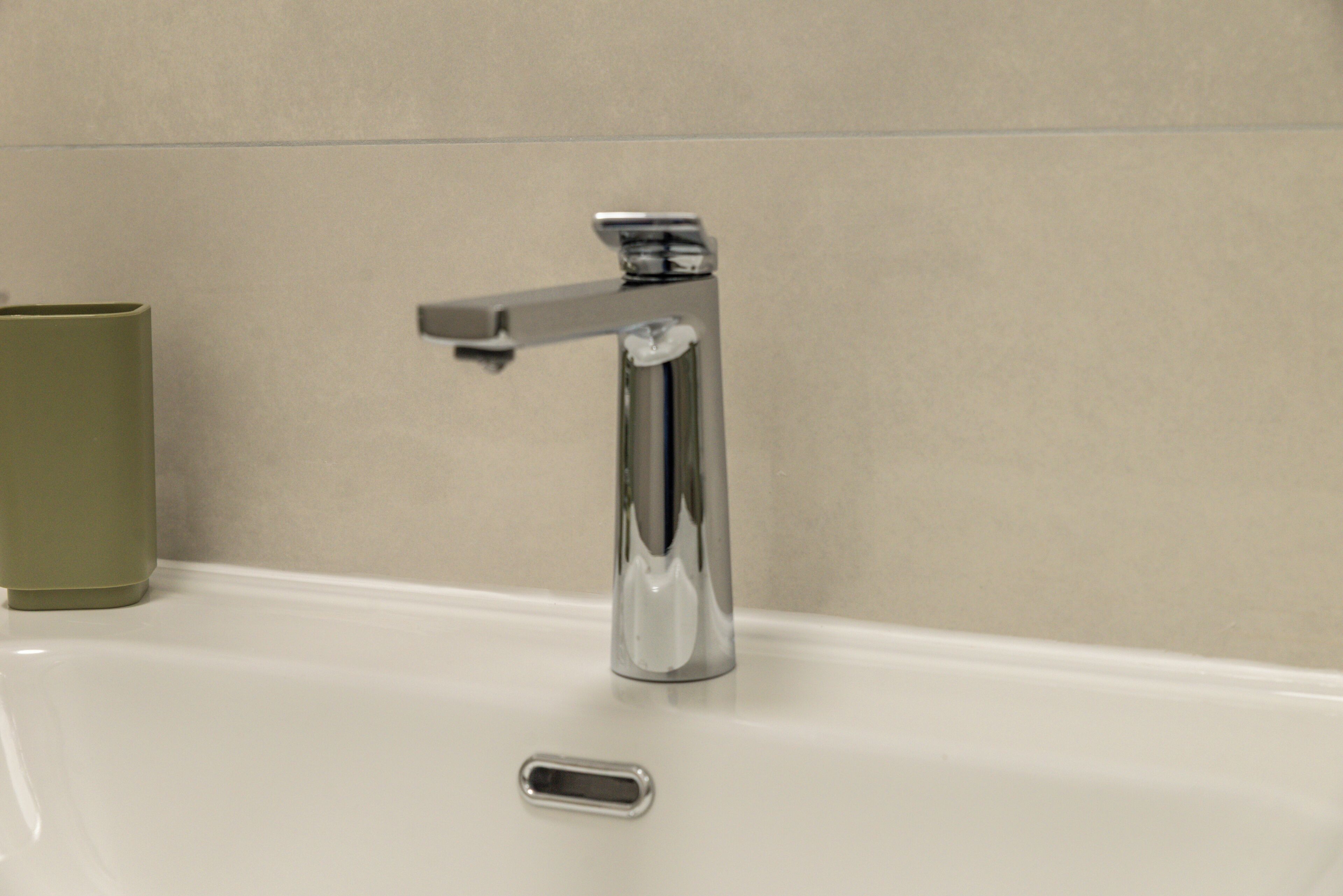 A bathroom with a chrome faucet, a white sink, and a green cup.