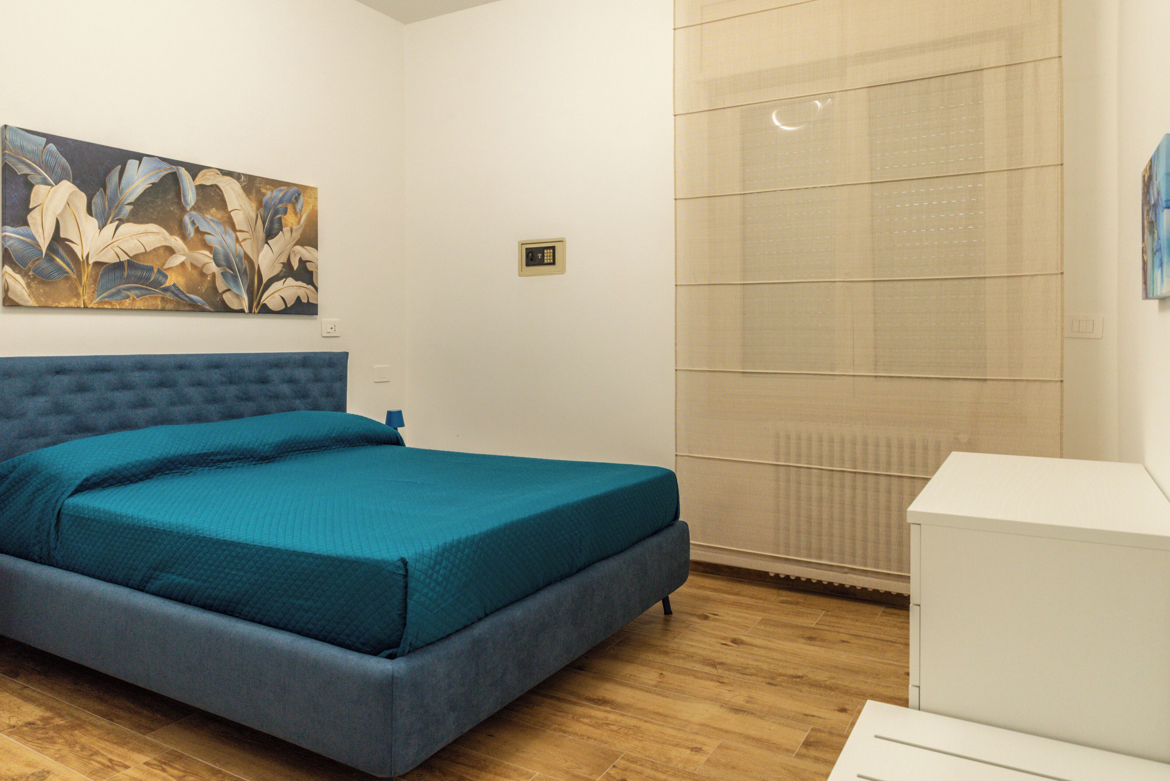 A bedroom with a bed, a painting on the wall, and a radiator.