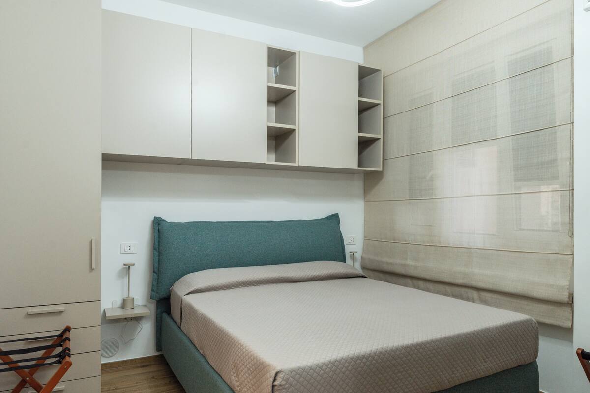 Un dormitorio con cama, armario, mesita de noche y ventana con persianas.