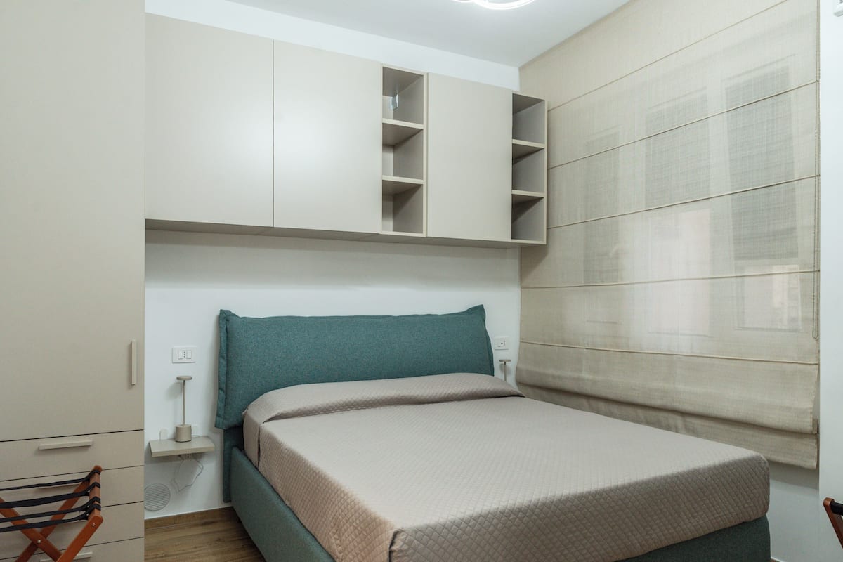 Une chambre à coucher comprenant un lit, une armoire, une table de chevet et une fenêtre avec des stores.