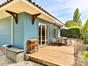 Ein blaues Haus mit einer Holzterrasse, einer Schiebetür und einem kleinen Tisch mit Stühlen.