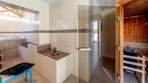 Un bany amb banyera, dutxa i una porta de vidre que dona a una zona de sauna de fusta.