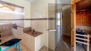 Ein Badezimmer mit Badewanne, Dusche und einer Glastür zum Holzsaunabereich.