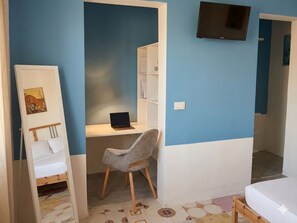 A bedroom with a bed, a desk with a laptop, a chair, a TV on the wall, and a bookshelf. - Aqua Home Area – Aqua Ground (Porto Cesareo)