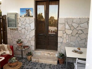 A stone-walled entrance with a wooden door, a small table with a chair, and potted plants. - Aqua Home Area – Aqua Ground (Porto Cesareo)