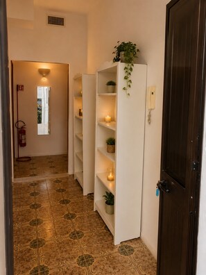 A hallway with patterned floor tiles, white shelving units with plants, a lit candle, and a dark wooden door. - Aqua Home Area - Core Four (Porto Cesareo)