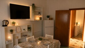 A dining area with a table set for two, a television mounted above, and a refrigerator to the right. - Aqua Home Area - Core Four (Porto Cesareo)