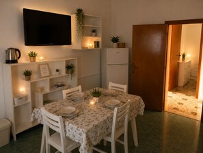 Ein Essbereich mit einem Tisch für zwei Personen, einem darüber hängenden Fernseher und einem Kühlschrank zur Rechten.