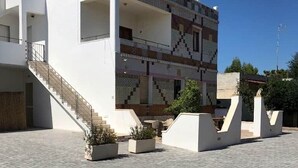 A modern building with a flat roof, a staircase leading to an upper level, and a paved courtyard. - Aqua Home Area – Core Five (Porto Cesareo)