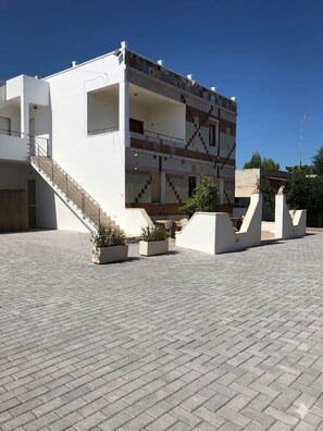 A modern building with a flat roof, a staircase leading to an upper level, and a paved courtyard. - Aqua Home Area – Core Five (Porto Cesareo)