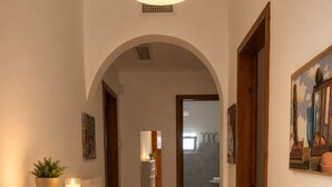 A hallway with patterned flooring, white shelving, a potted plant, a lit candle, and a painting on the wall. - Aqua Home Area – Core Five (Porto Cesareo)