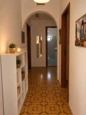 A hallway with patterned flooring, white shelving, a potted plant, a lit candle, and a painting on the wall. - Aqua Home Area – Core Five (Porto Cesareo)