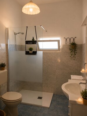 A modern bathroom with a glass shower enclosure, a toilet, a sink, and a small window providing natural light. - Aqua Home Area – Core Five (Porto Cesareo)