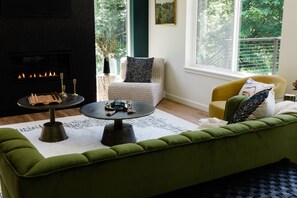 A cozy living room with a fireplace, a green sofa, a yellow armchair, and a chessboard. - Emerald Acres, an elevated Retreat on Five Private Acres (Bellingham)