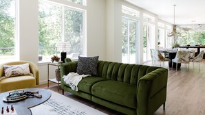 Ein geräumiger Wohnbereich mit einem grünen Sofa, einem gelben Sessel und einem Esstisch mit Stühlen.