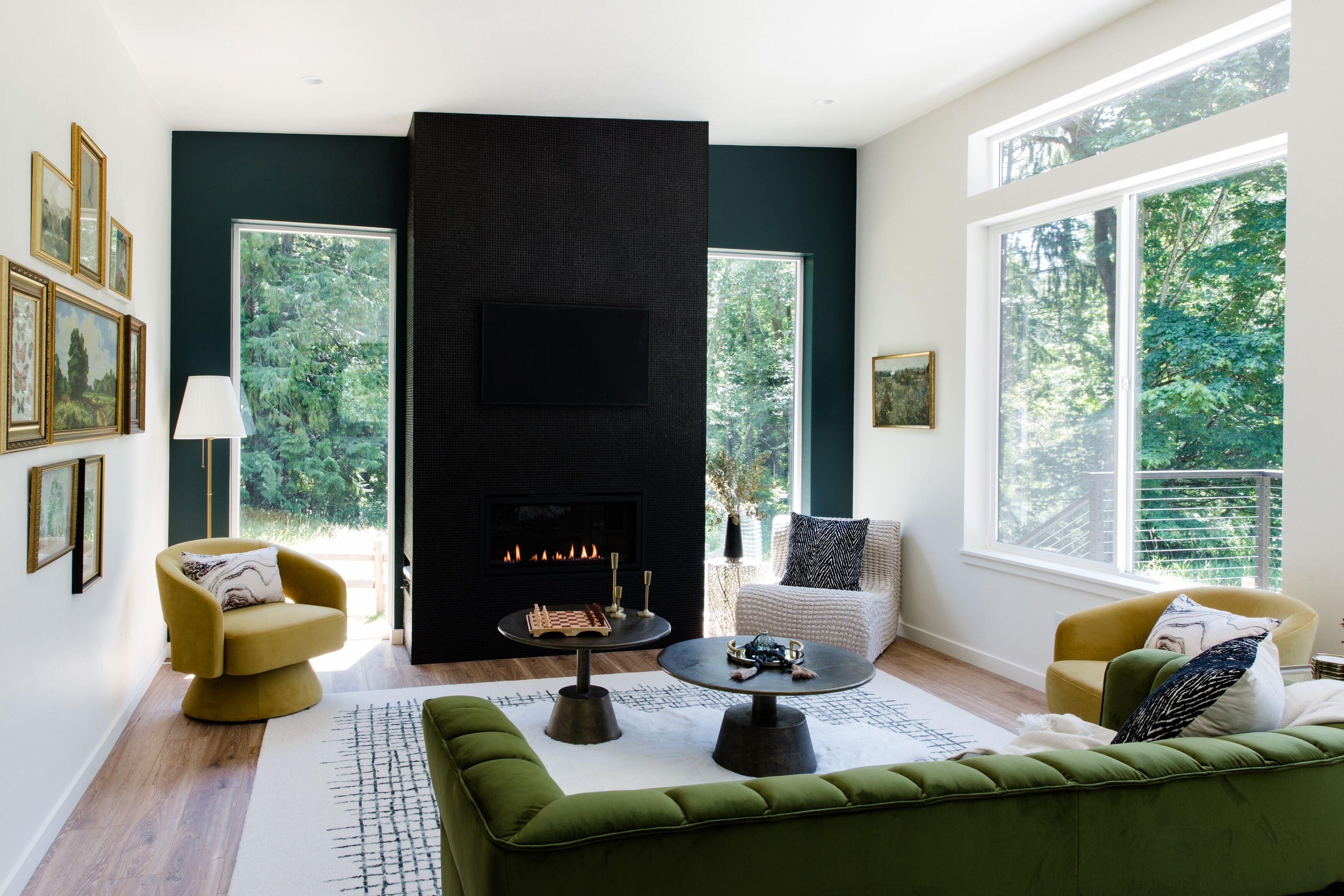 Un salon moderne avec une cheminée, un canapé vert, des fauteuils et de grandes fenêtres.