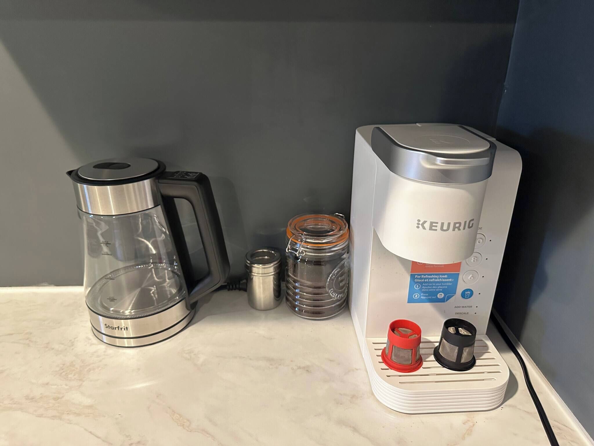 Una cafetera Keurig con depósito de agua, una jarra de vidrio y una jarra metálica sobre una encimera de cocina.
