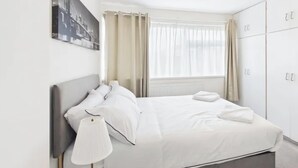 A modern hotel room with a bed, a bedside lamp, a window with curtains, and a wardrobe. - 3 Bedroom Home with Private Garden in Newcastle (Whickham)