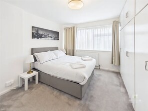 A modern hotel room with a bed, bedside table, lamp, and a cityscape painting. - 3 Bedroom Home with Private Garden in Newcastle (Whickham)