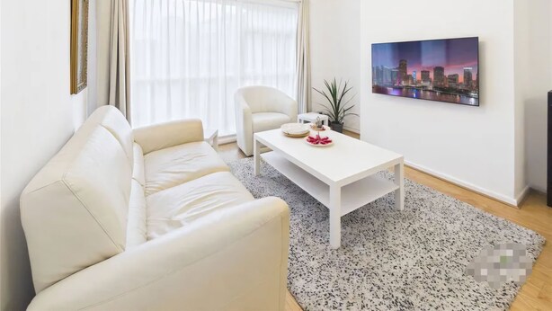 A modern living room with a white sofa, a coffee table, a cityscape painting, and a chandelier. - 3 Bedroom Home with Private Garden in Newcastle (Whickham)