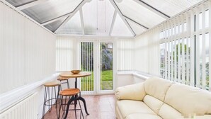 A conservatory with a glass ceiling, a round wooden table with stools, a beige sofa, and a view of the garden outside. - 3 Bedroom Home with Private Garden in Newcastle (Whickham)