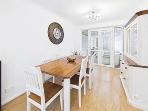 A dining area with a wooden table and white chairs, a wall clock, and a view through glass doors to a balcony. - 3 Bedroom Home with Private Garden in Newcastle (Whickham)