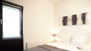 Ein Schlafzimmer mit einem Bett, einem Heizkörper, einem Fenster mit Jalousien und einem Wandbild.