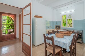 Eine Küche mit Esstisch, Stühlen, einem Kühlschrank und einem Fenster mit Blick auf Grünflächen.