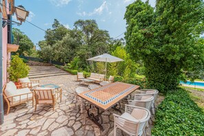 An outdoor patio with a table and chairs, surrounded by greenery and a pool. - Holiday Villa 'Villa Son Perot' with Mountain Views, Private Pool and Wi-Fi (Orient)