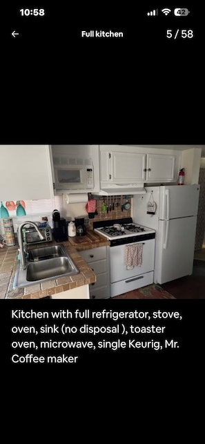 A compact kitchen with a full refrigerator, stove, oven, sink, toaster oven, microwave, single Keurig, and Mr. Coffee maker.