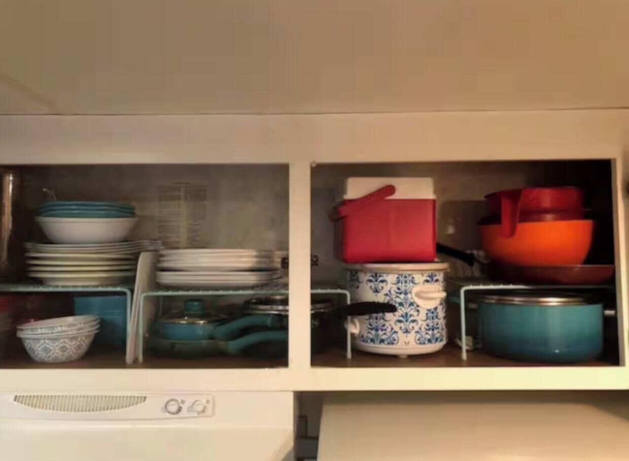 A kitchen cabinet with stacked dishes, pots, and a red pot on the right.